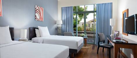 A hotel room with two beds, a desk with a TV, a chair, and a view of the outdoors.