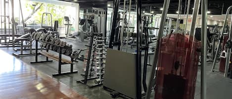 Un gimnasio con diferentes equipos de ejercicio, piso de madera y ventanas grandes que dejan entrar luz natural.
