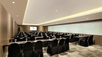 A conference room with multiple tables, chairs, and a large screen.