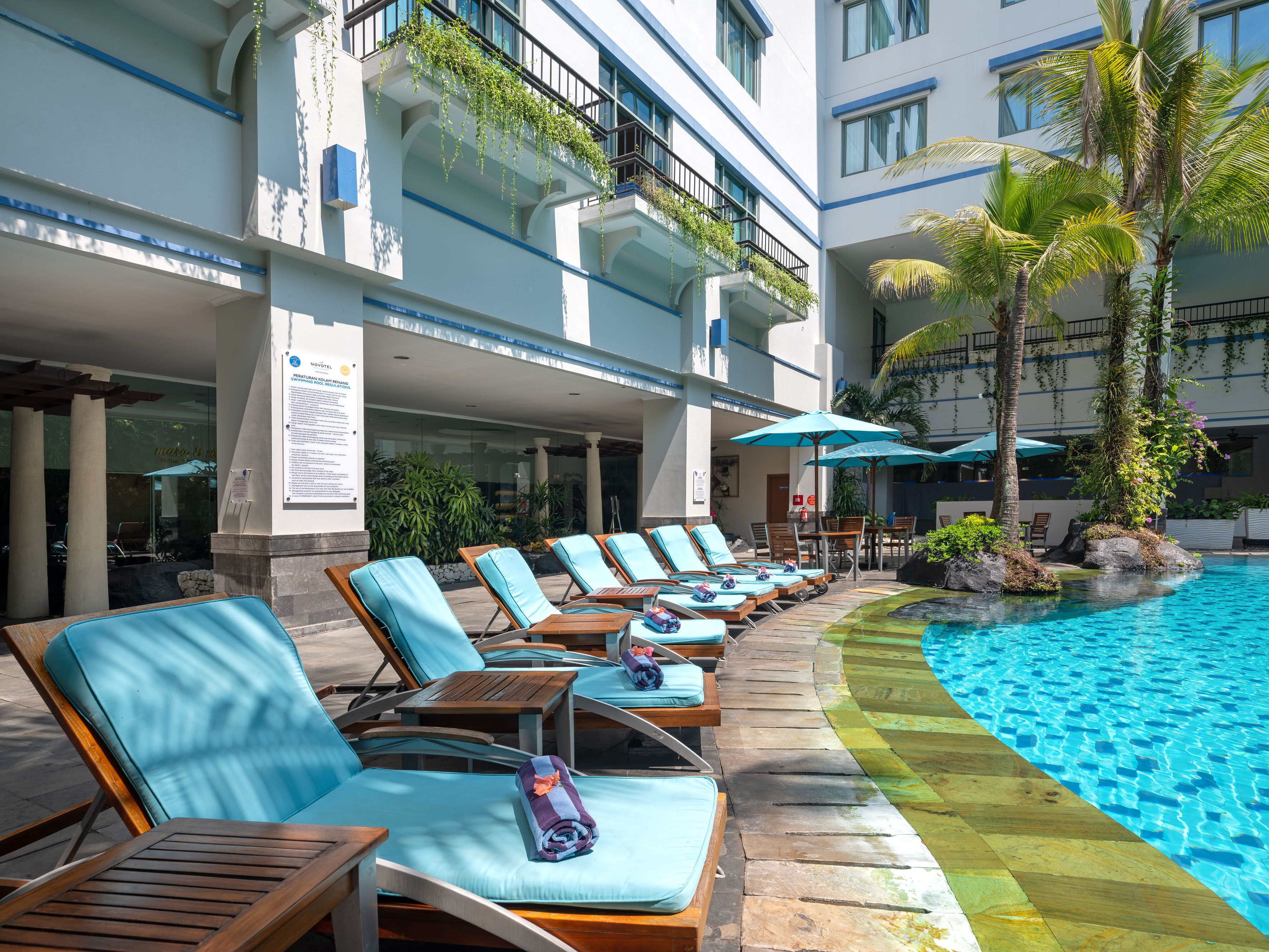 A poolside area with lounge chairs and umbrellas, a clear blue pool, and a building with balconies.
