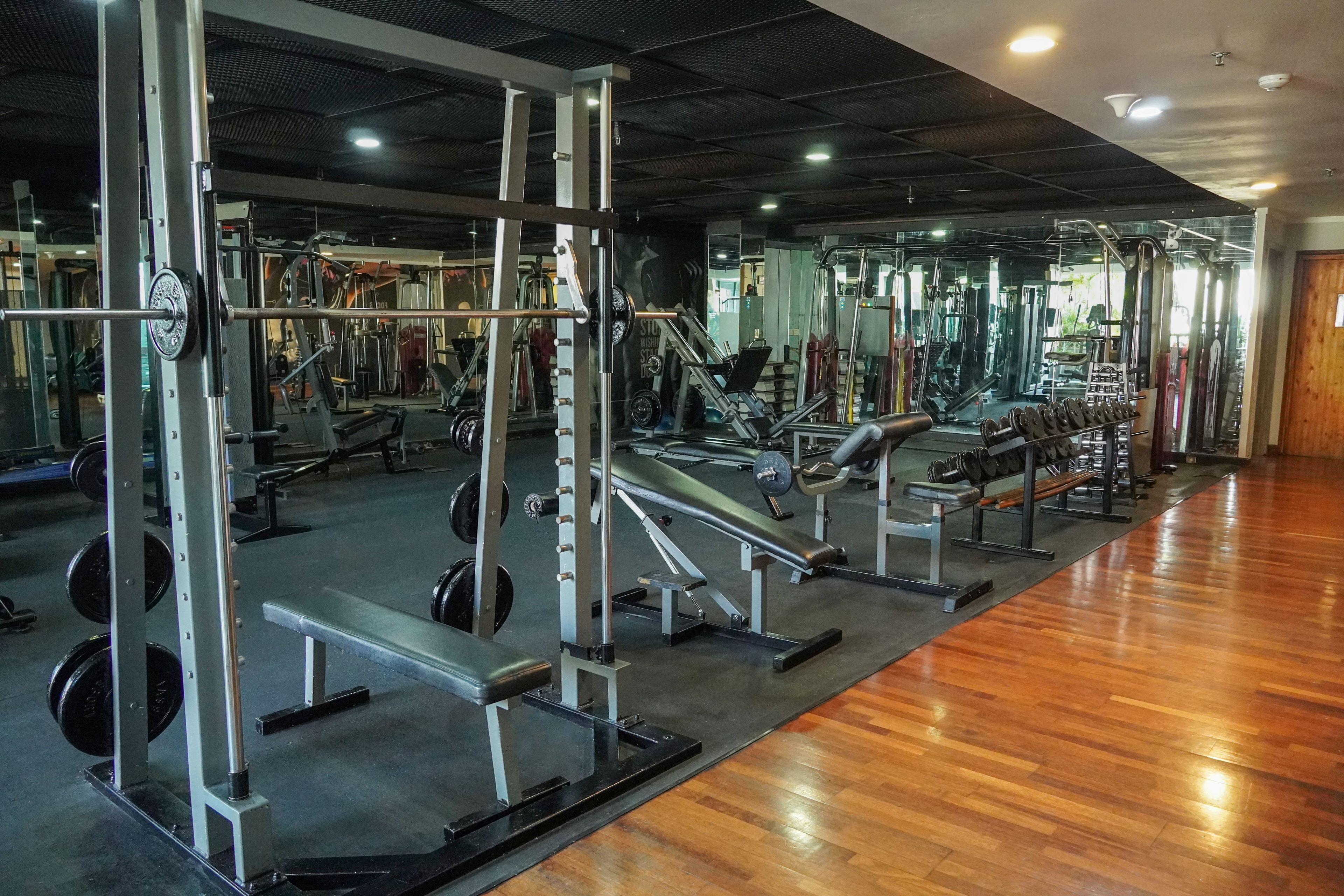 Une salle de sport équipée de divers appareils de musculation, de bancs et d’un mur recouvert de miroirs.