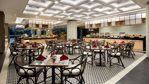 Un restaurante con diseño moderno, que presenta un suelo con estampado, varias mesas de comedor con sillas y un techo alto con tragaluces.