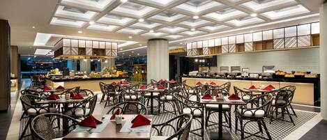 Un restaurante con diseño moderno, que presenta un suelo con estampado, varias mesas de comedor con sillas y un techo alto con tragaluces.