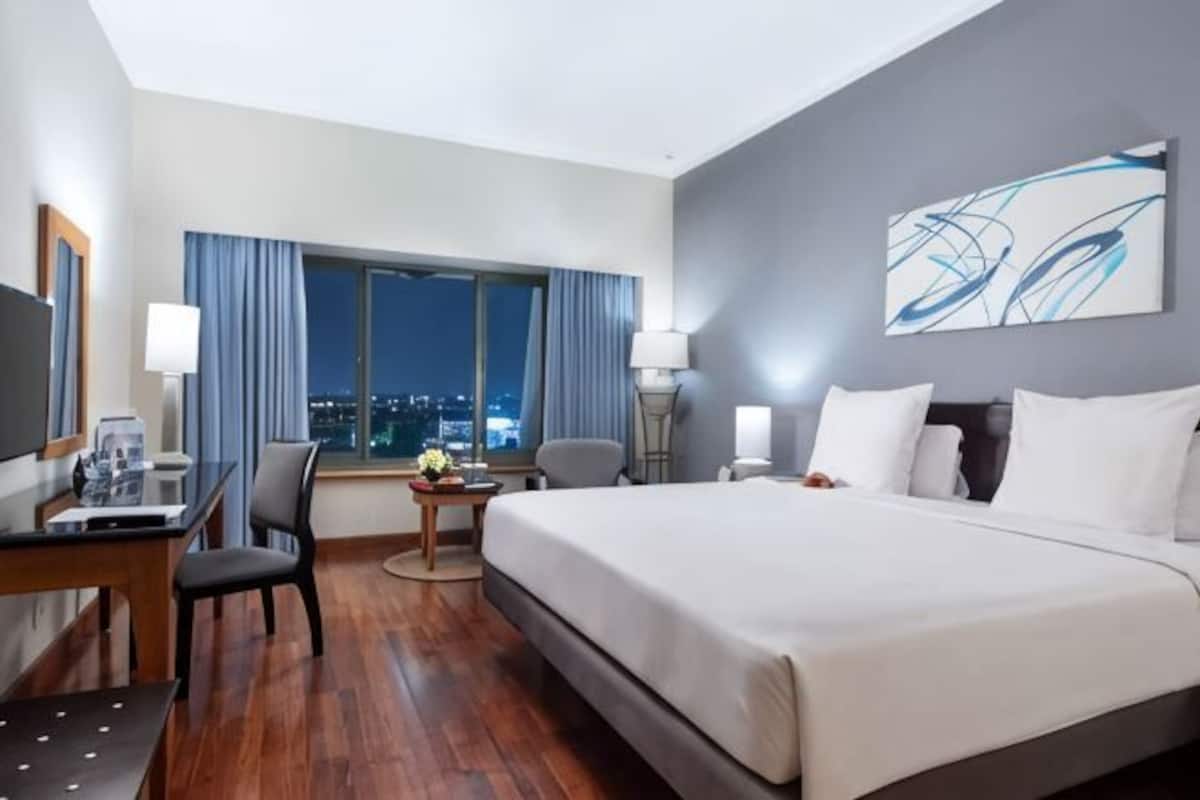 A hotel room with a large bed, a desk with a chair, a TV, and a window with curtains.