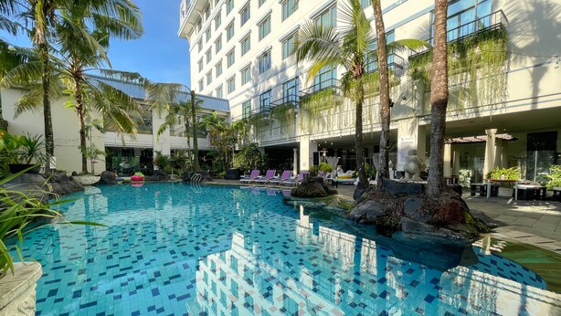 Un hotel con piscina rodeada de palmeras y sillas de descanso.