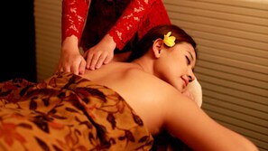 A person receiving a massage in a room with a patterned blanket and a red garment. - Kimaya Sudirman Yogyakarta by Harris (Yogyakarta)
