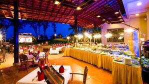 An outdoor dining area with tables set for a meal, a buffet with various food items, and a covered seating area with a view of the surrounding landscape.
