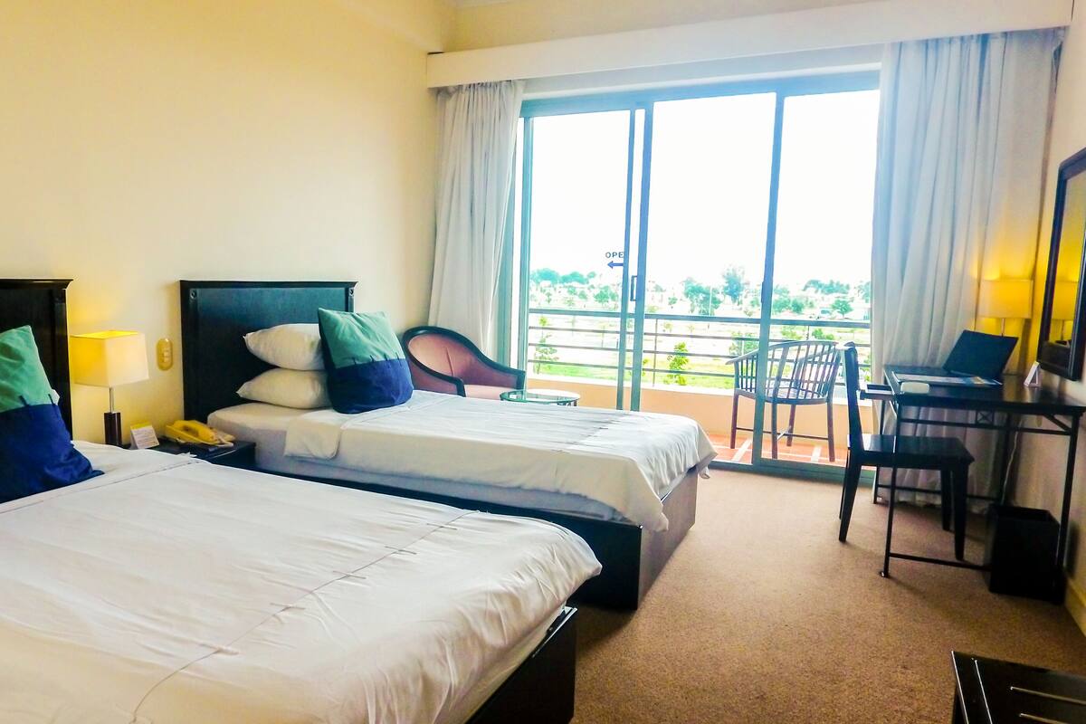 Une chambre d’hôtel avec deux lits, un bureau avec un ordinateur portable, une chaise et une vue sur l’extérieur.