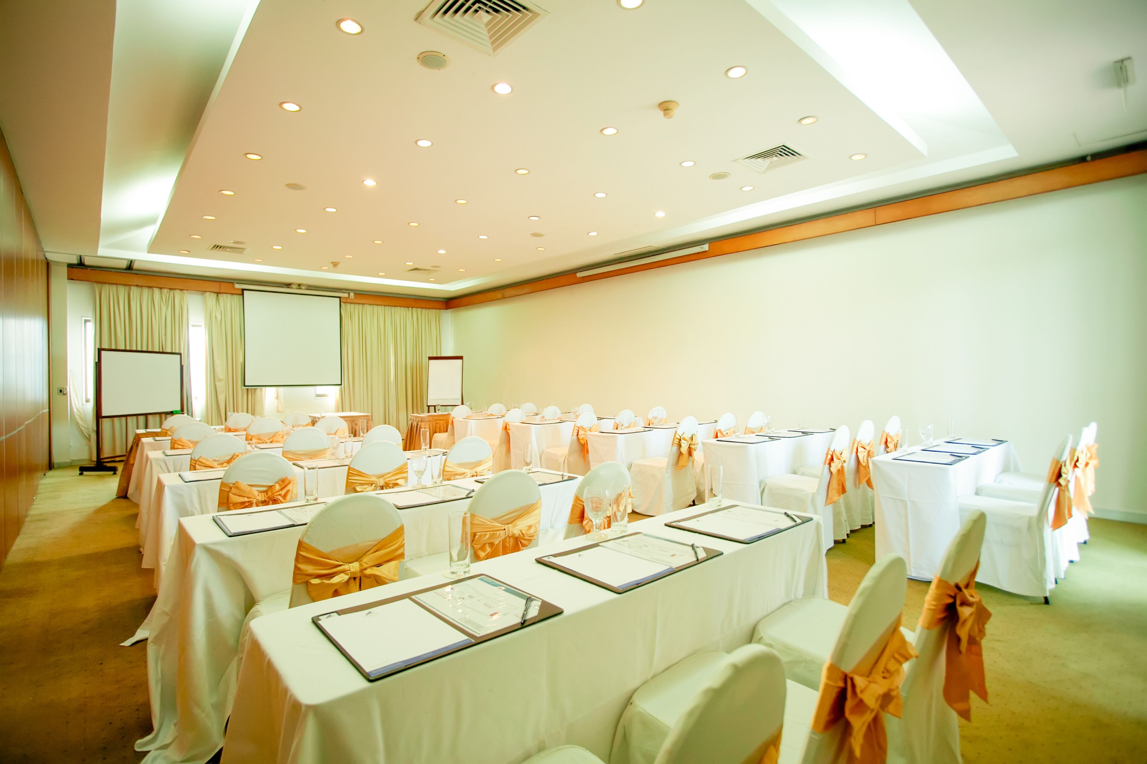 A conference room with rows of tables, white tablecloths, and chairs with orange sashes.