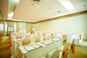 A conference room with rows of tables, white tablecloths, and chairs with orange sashes.