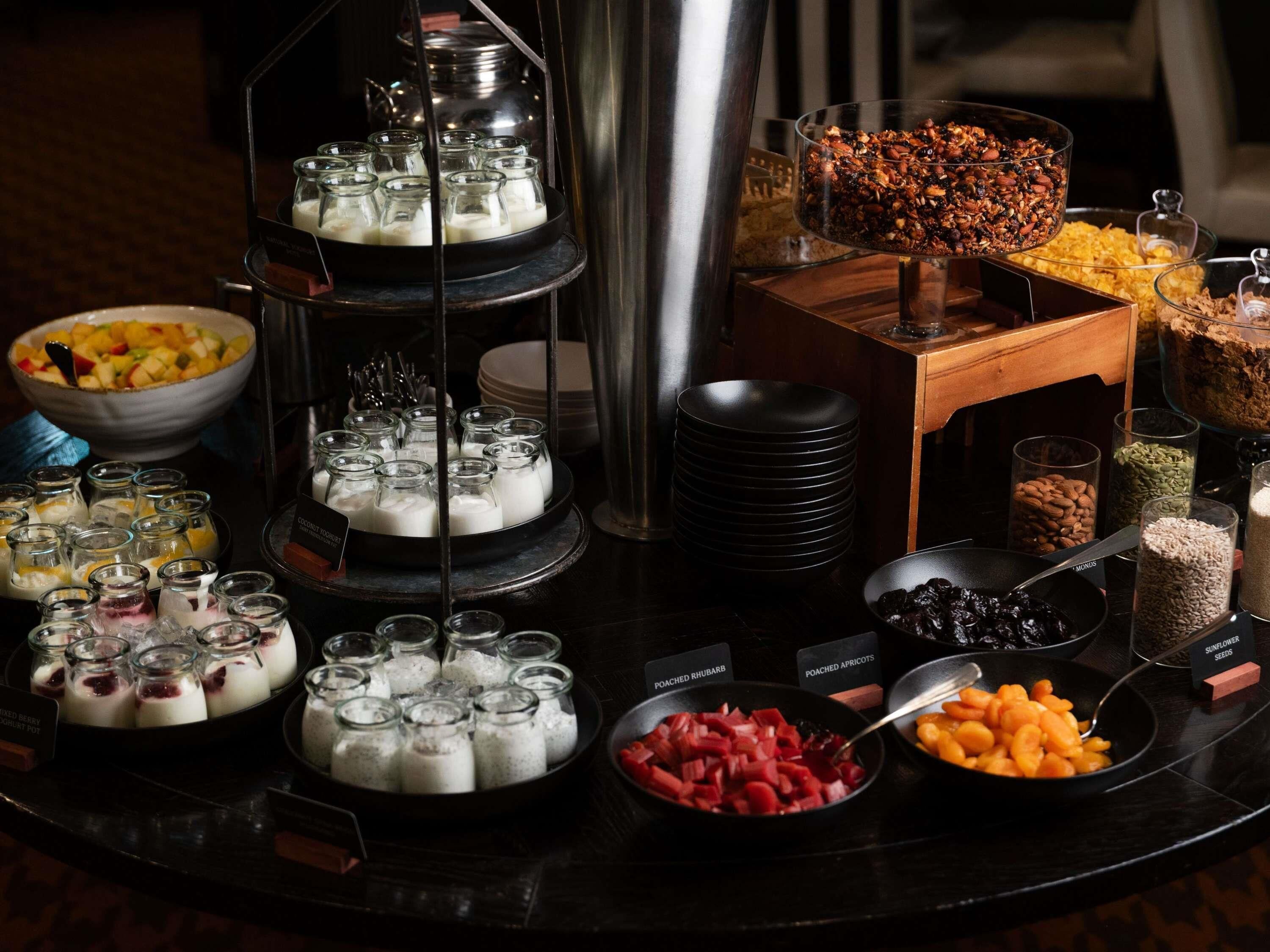 Un buffet proposant une variété d’aliments, notamment des yaourts, des fruits, des noix et des fruits pochés.