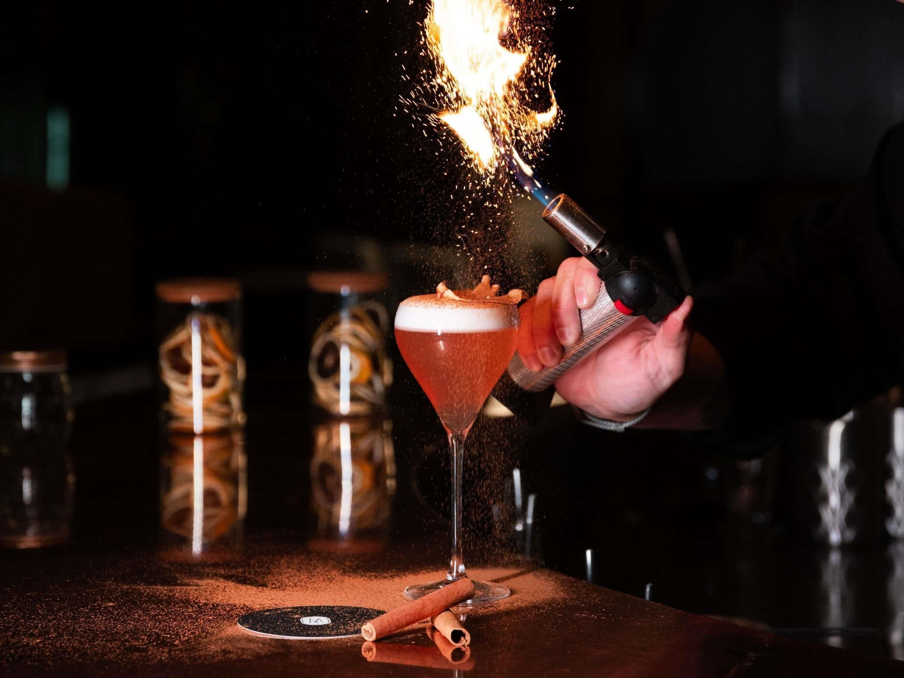 A bartender pouring a drink into a martini glass with a flaming effect.