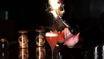 A bartender pouring a drink into a martini glass with a flaming effect.