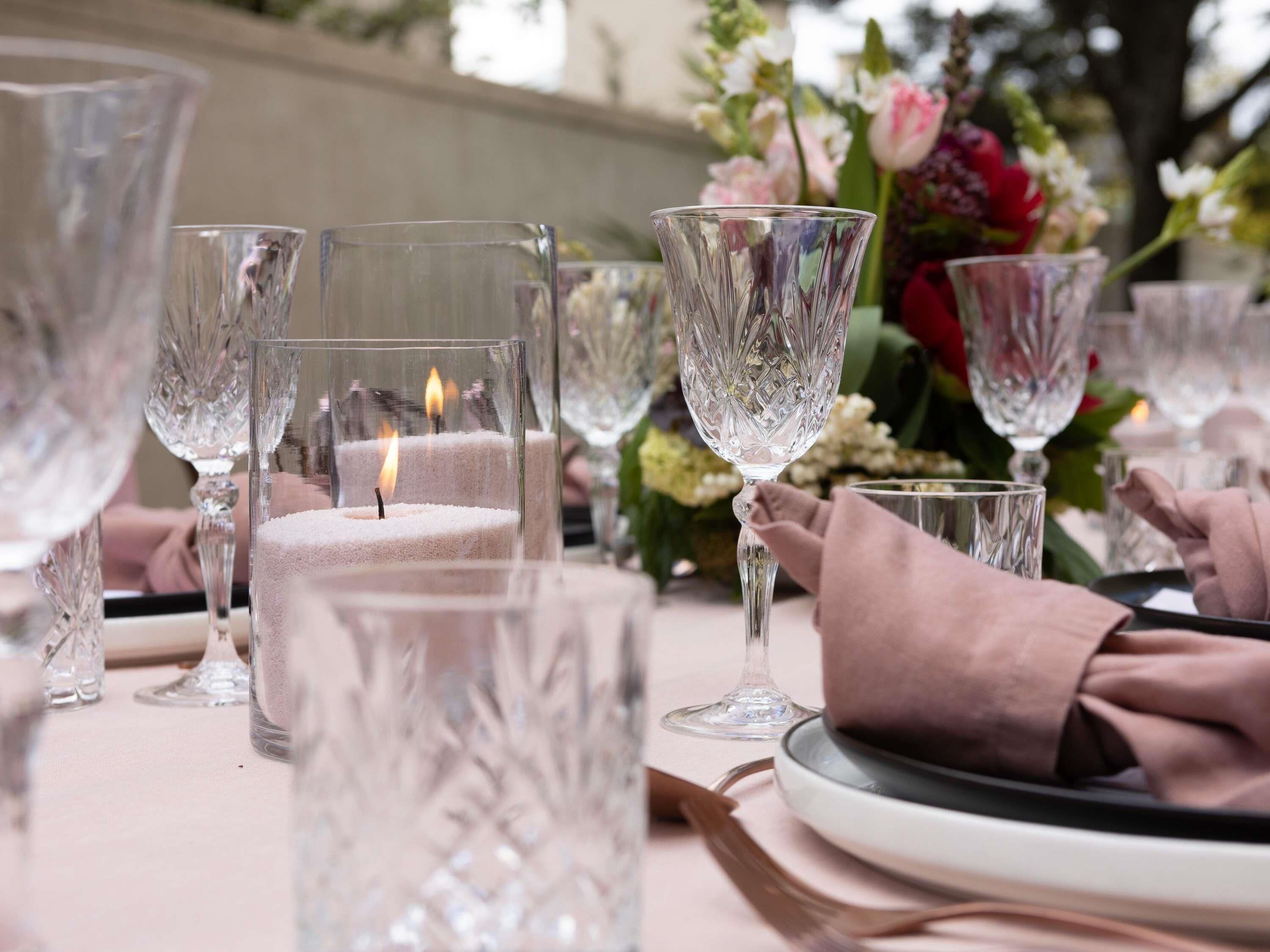 A table set with crystal glasses, a lit candle, and a floral arrangement.