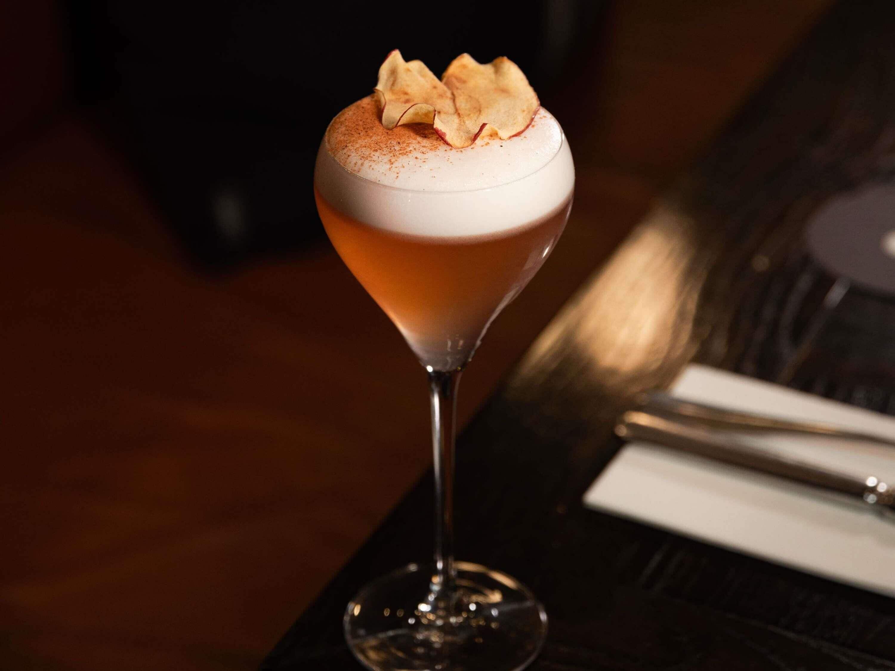 Un cocktail servi dans un verre à martini, avec une mousse onctueuse et une pincée d’épices saupoudrée sur le dessus.