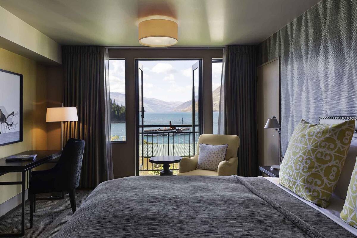 Ett hotellrum med en stor säng, ett skrivbord, en stol och utsikt över havet.