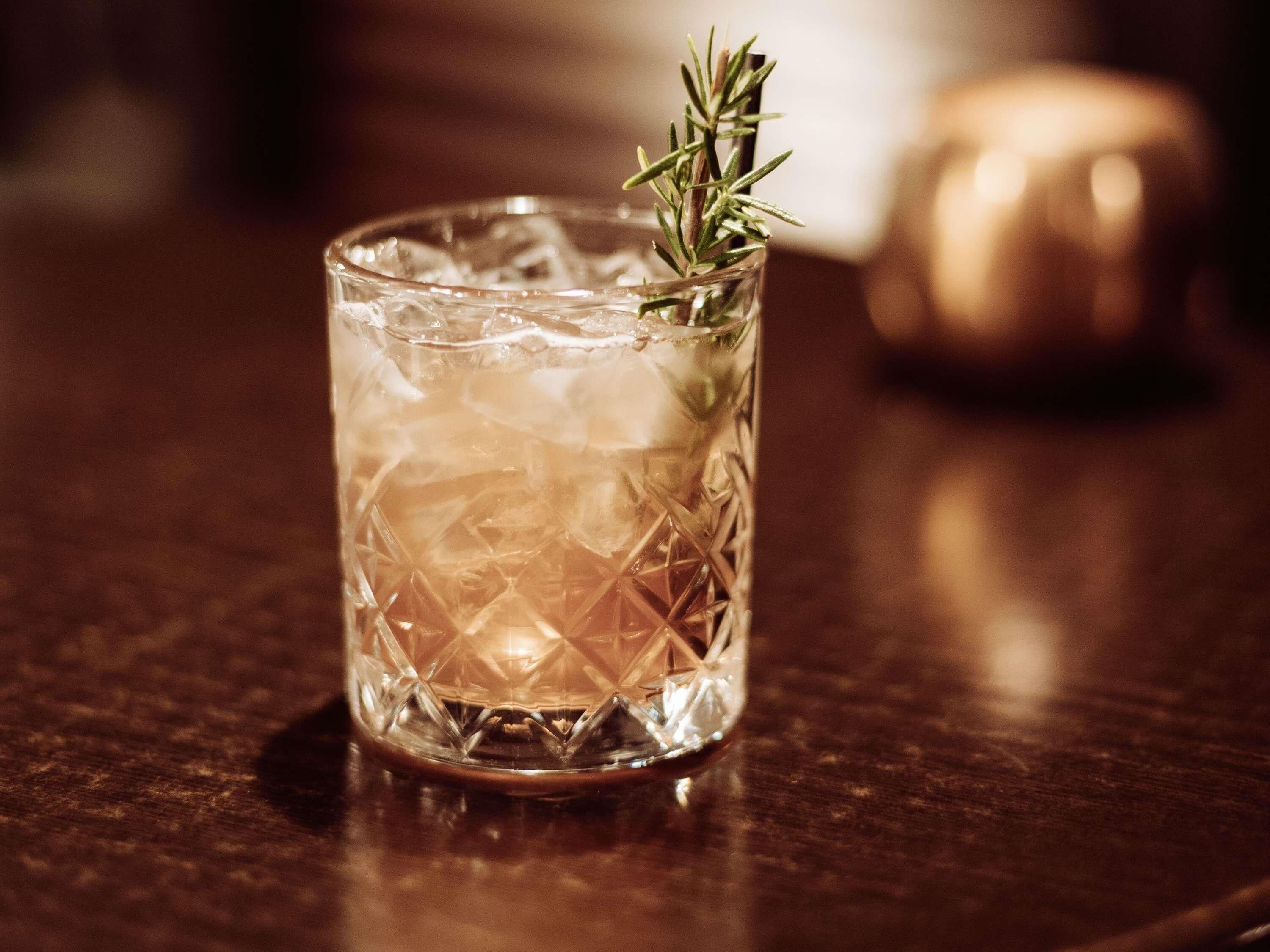 A clear glass with a geometric pattern, containing a sprig of rosemary, placed on a wooden surface.