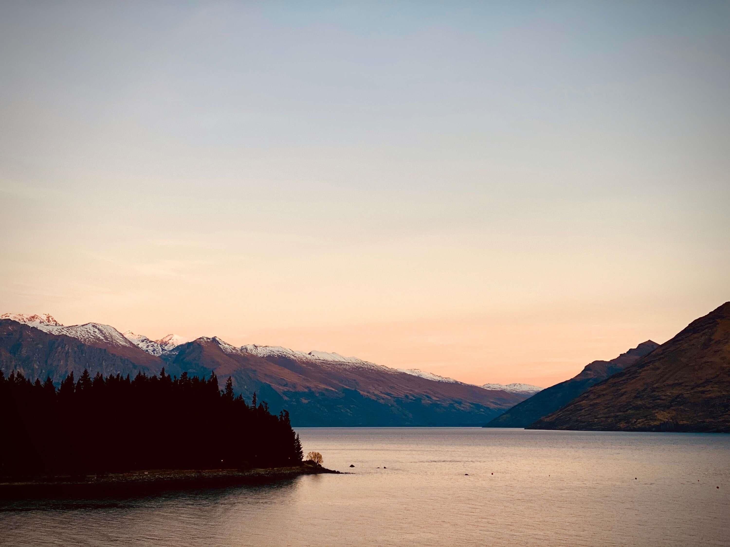 A calm lake with mountains in the background and a forested shoreline.