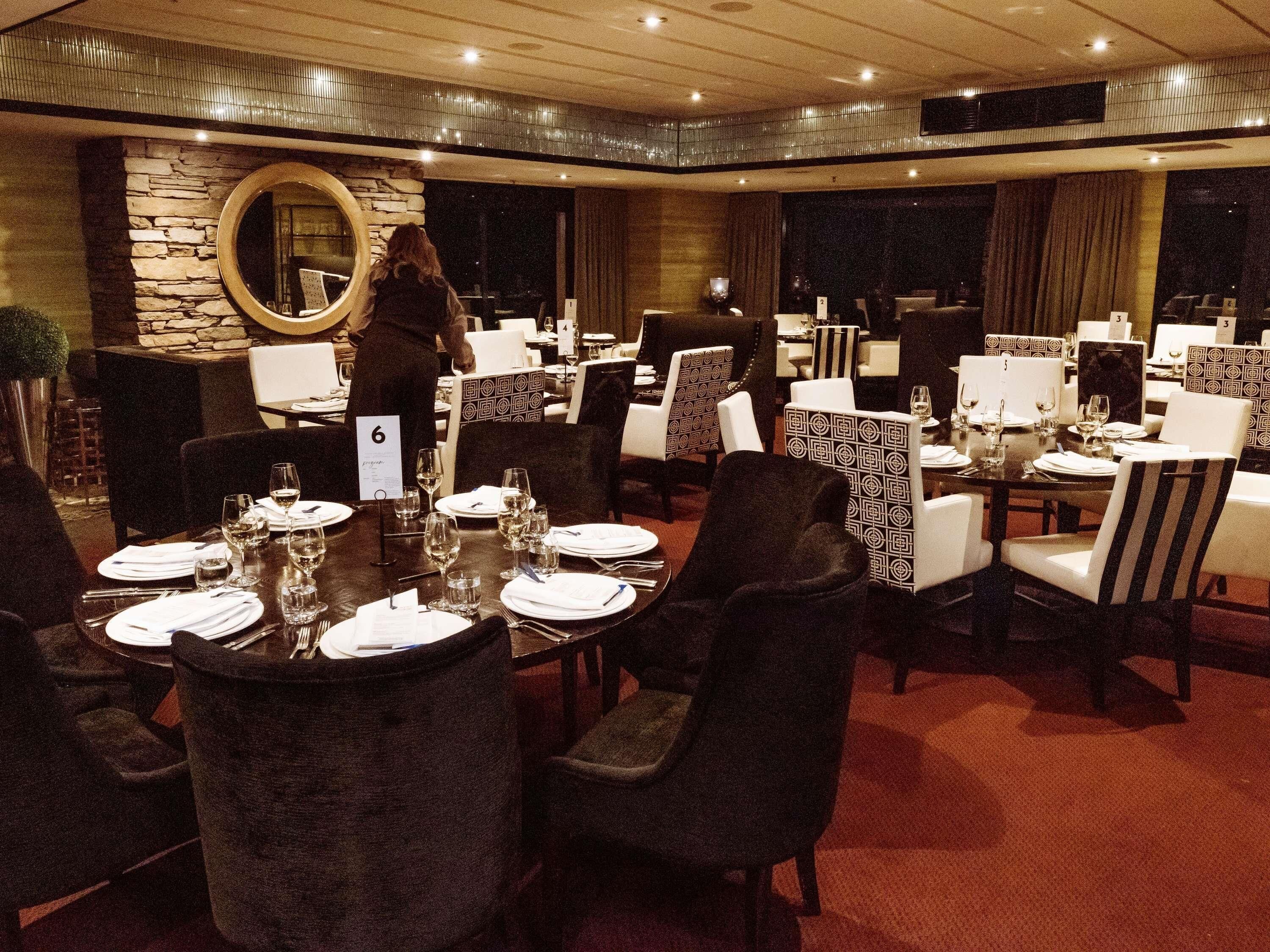 Un restaurante con mesas redondas, sillas de estampado blanco y negro y una pared de piedra con un espejo.