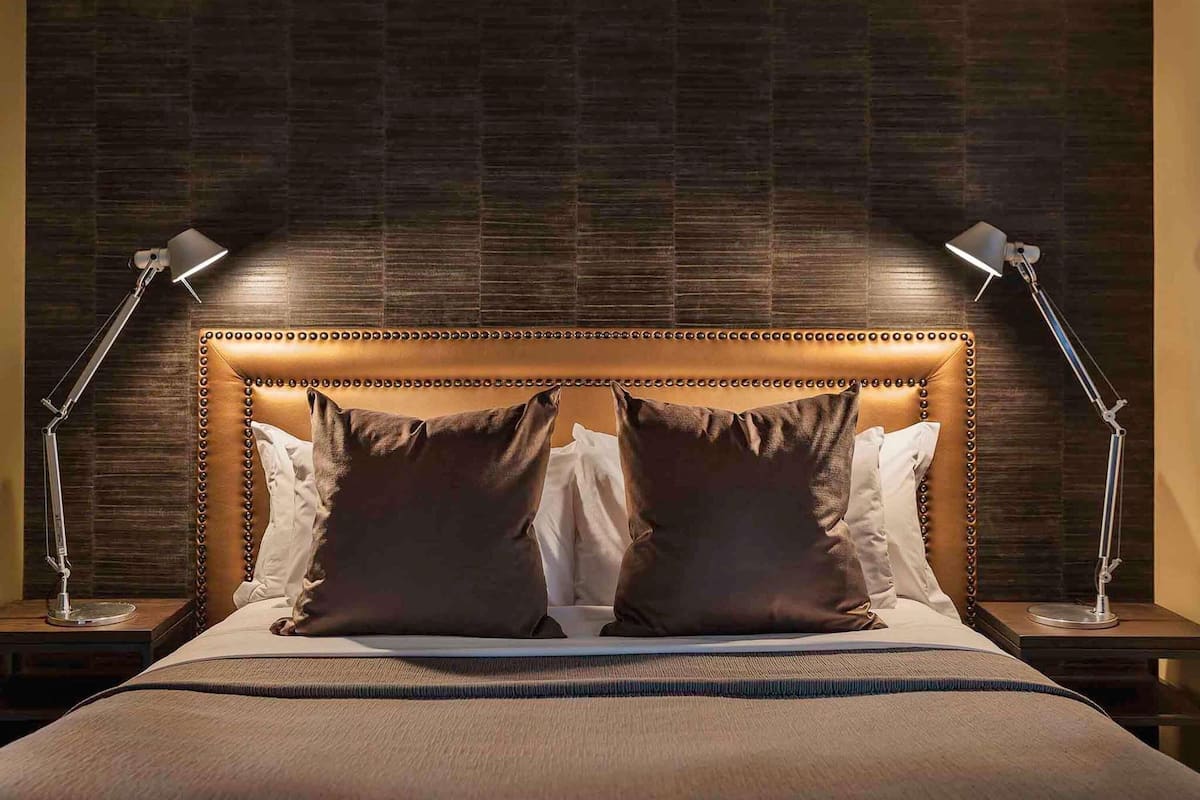 Ein Bett mit einem karossierten Kopfteil, zwei Nachttischlampen und einer Wand mit dunklem Muster.