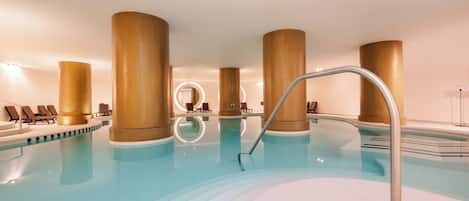 An indoor swimming pool with multiple lanes, lounge chairs, and a central circular viewing area.