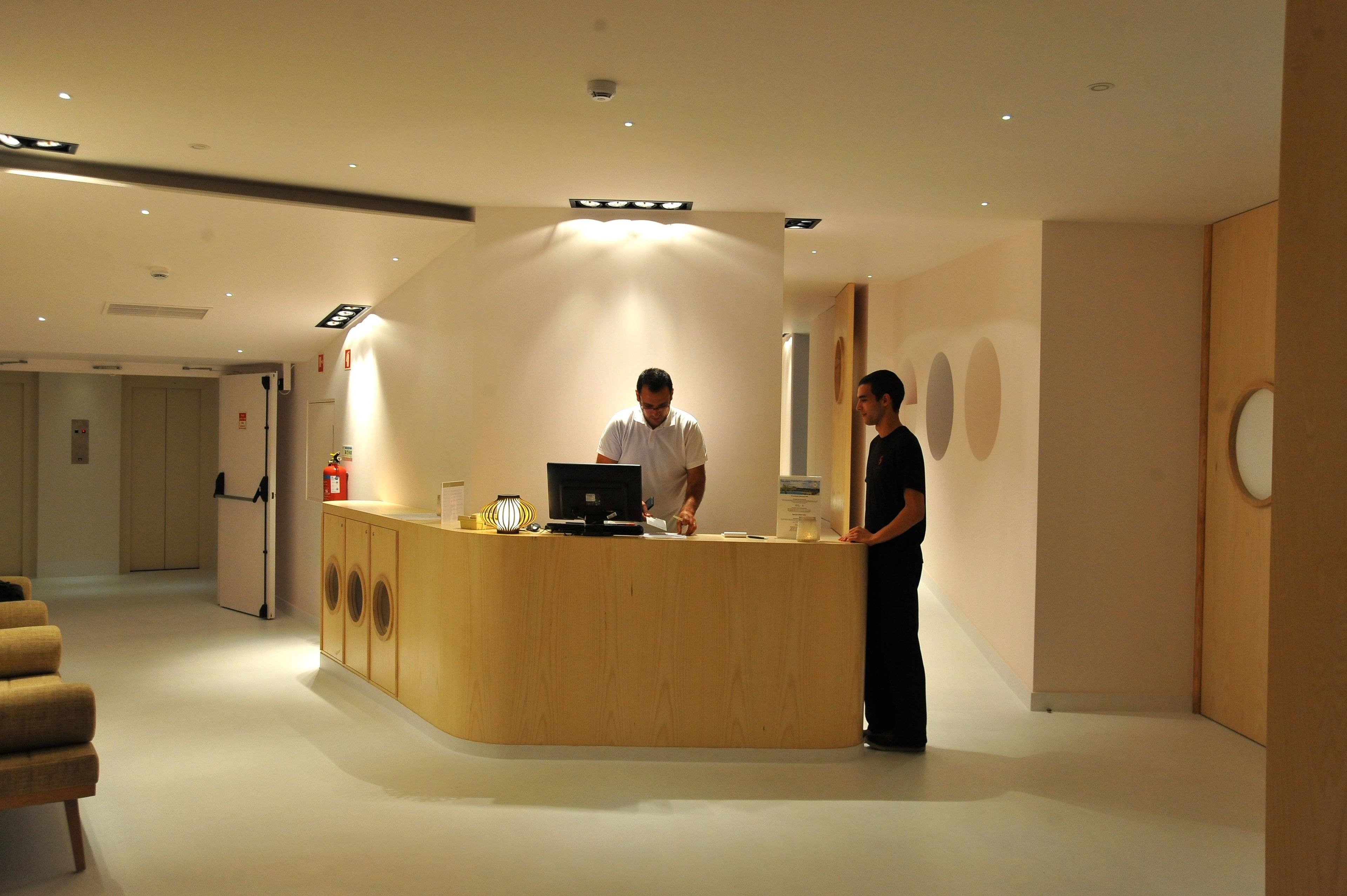 A reception desk with a computer and a fire extinguisher. There are two people standing near the desk.
