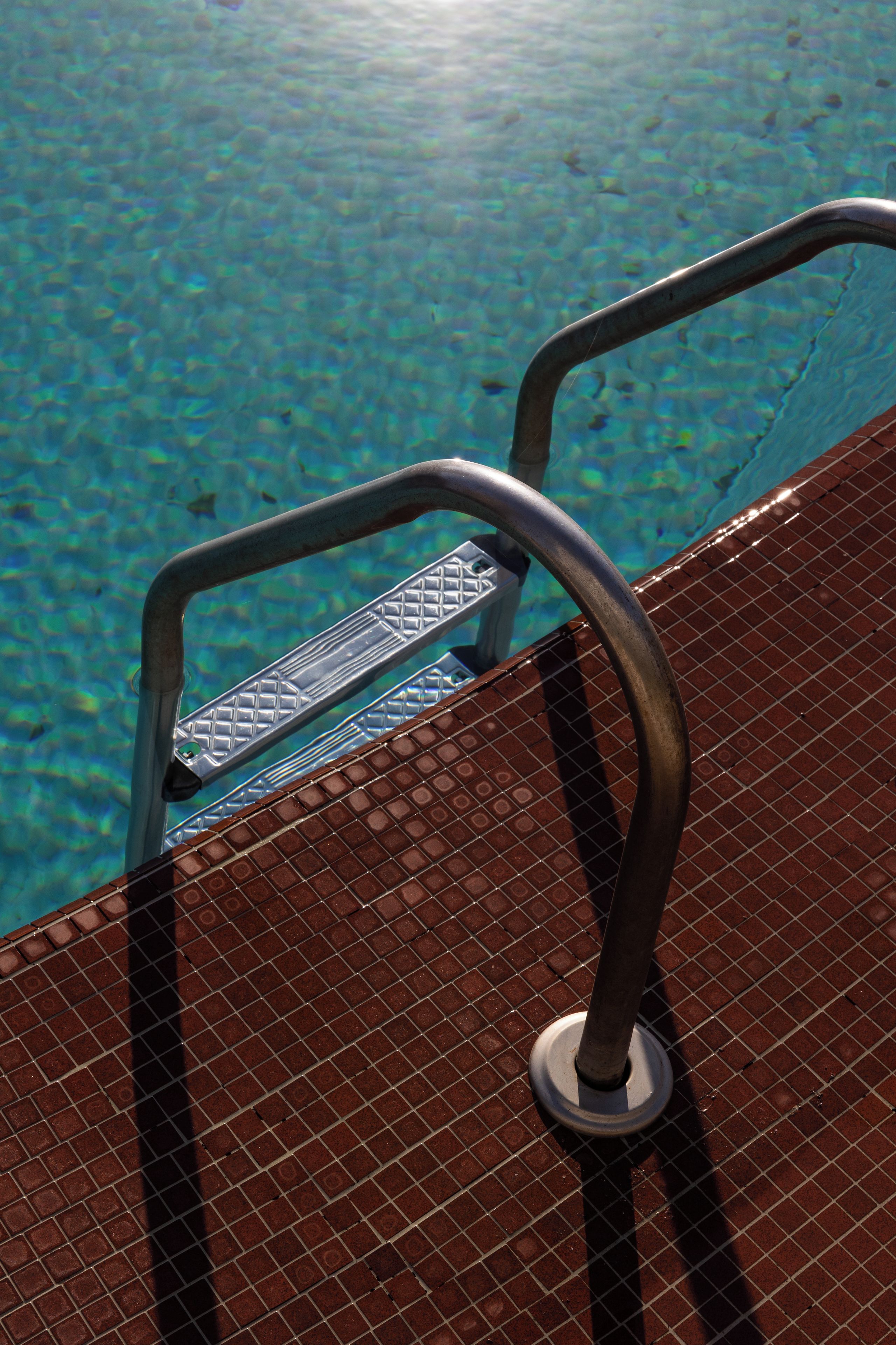 Una escalera metálica para piscina con superficie texturizada, que da acceso a una piscina con agua cristalina.