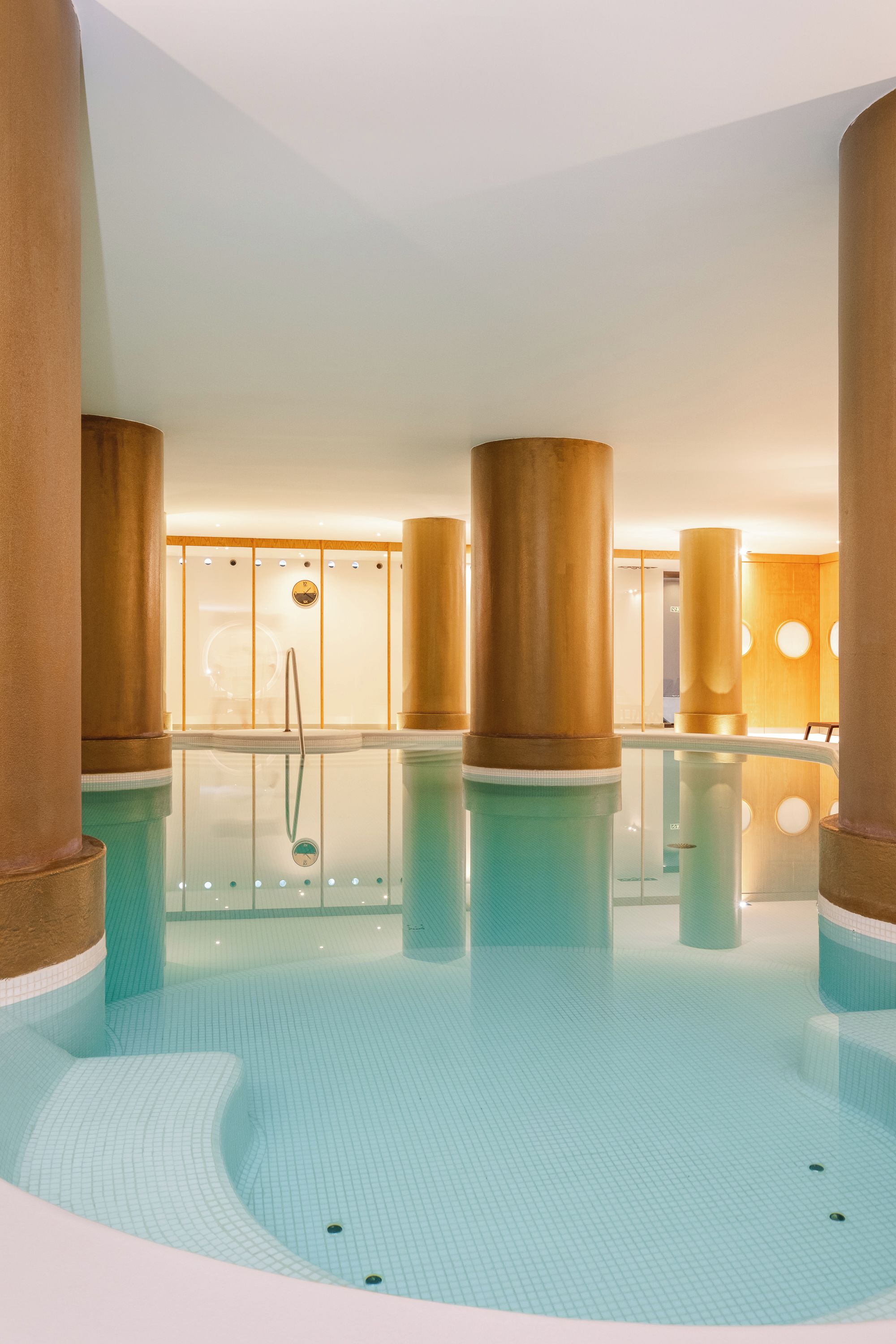 Una piscina interior con agua cristalina, rodeada de grandes columnas cilíndricas y un suelo de baldosas.