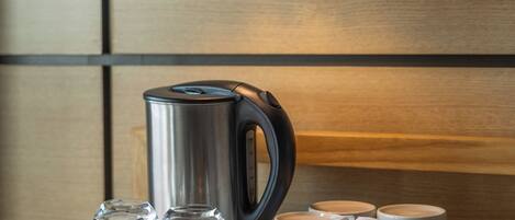 A neatly arranged table with a kettle, glasses, and a mug holder. A wall-mounted lamp provides light.