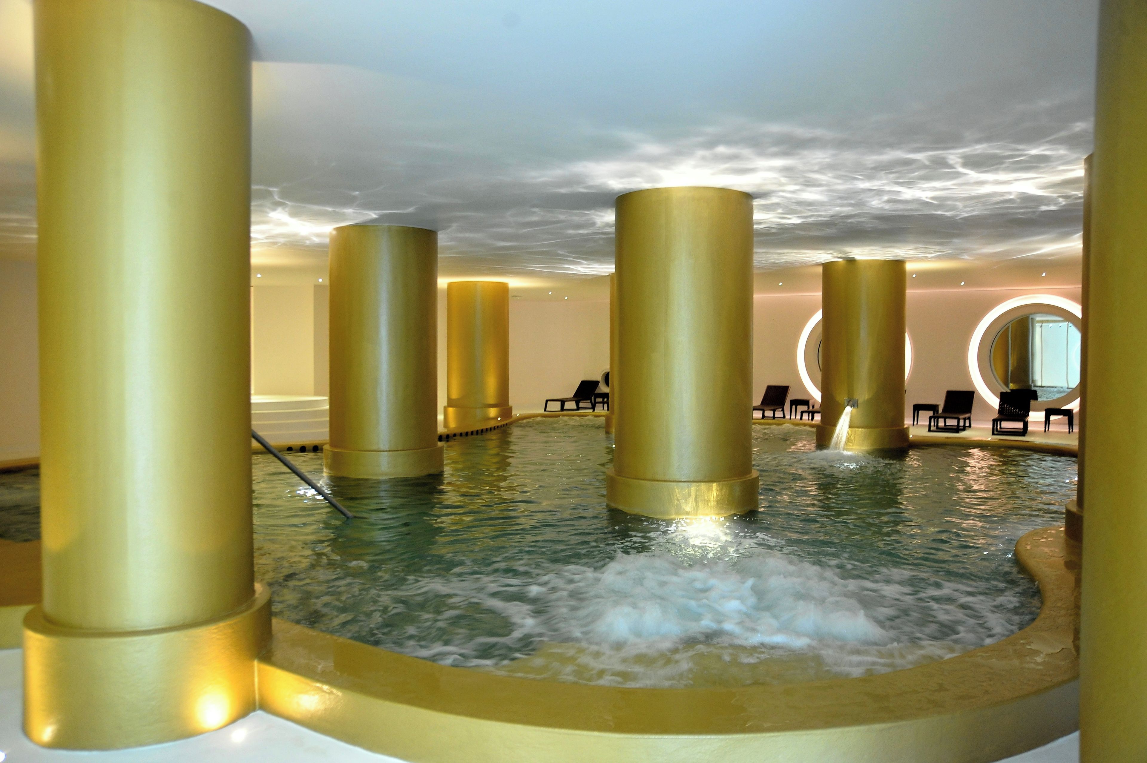 Un área de spa con un jacuzzi rodeado de pilares dorados, una zona de estar circular y vistas al cielo.