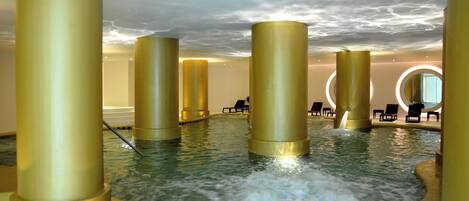 Un área de spa con un jacuzzi rodeado de pilares dorados, una zona de estar circular y vistas al cielo.