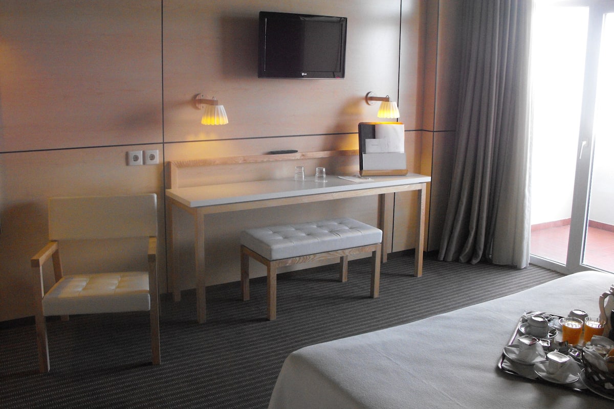 A hotel room with a bed, a desk, a chair, a TV, and a breakfast tray.