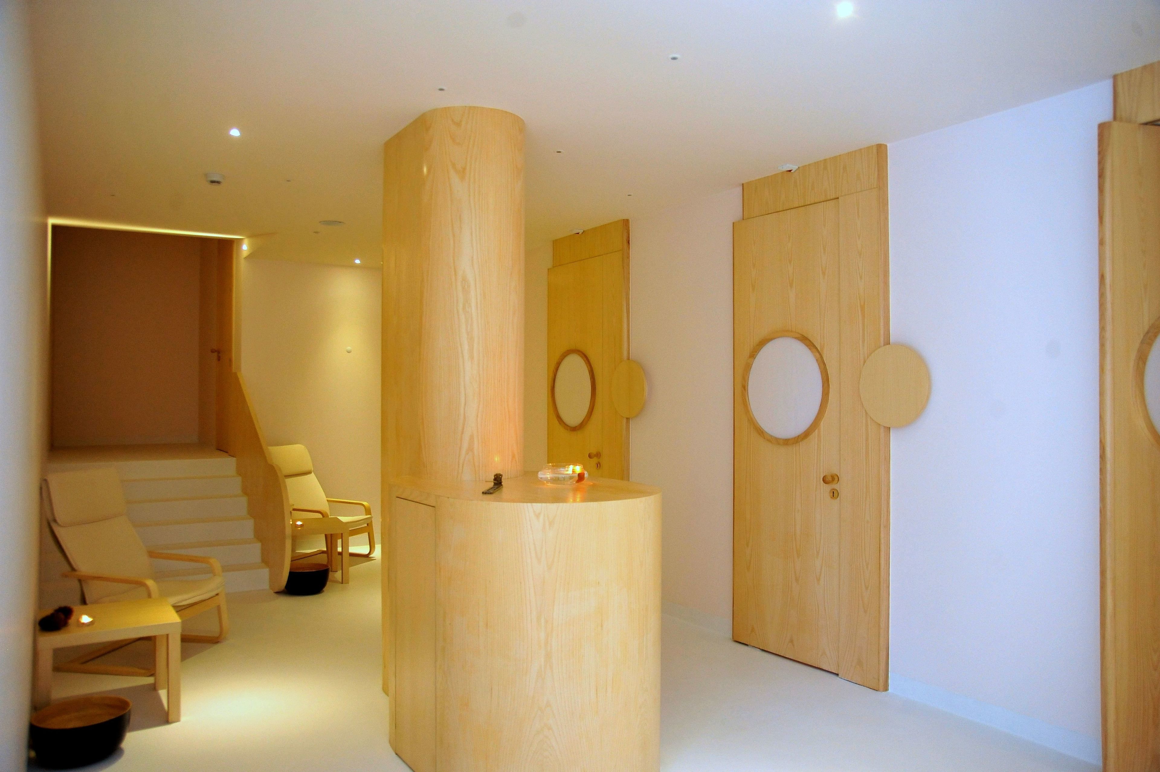 A modern interior with a wooden reception desk, a staircase, and a seating area with chairs.