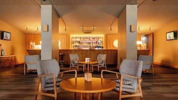 Een bar met houten meubels, een ronde tafel en een plank met flessen.