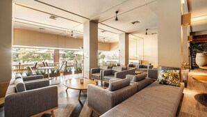 Un espace de détente moderne, doté de canapés, de fauteuils et d’une table basse, avec de grandes fenêtres offrant une vue sur l’extérieur.