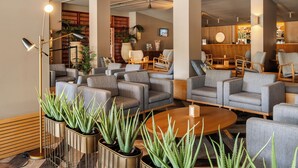 Un espace de détente moderne avec des canapés et des fauteuils, une table basse en bois et des plantes d’aloès en pot.