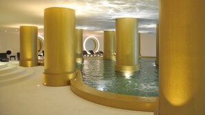 A luxurious indoor pool area with golden columns and lounge chairs. - Axis Vermar Conference & Beach Hotel (Povoa De Varzim)