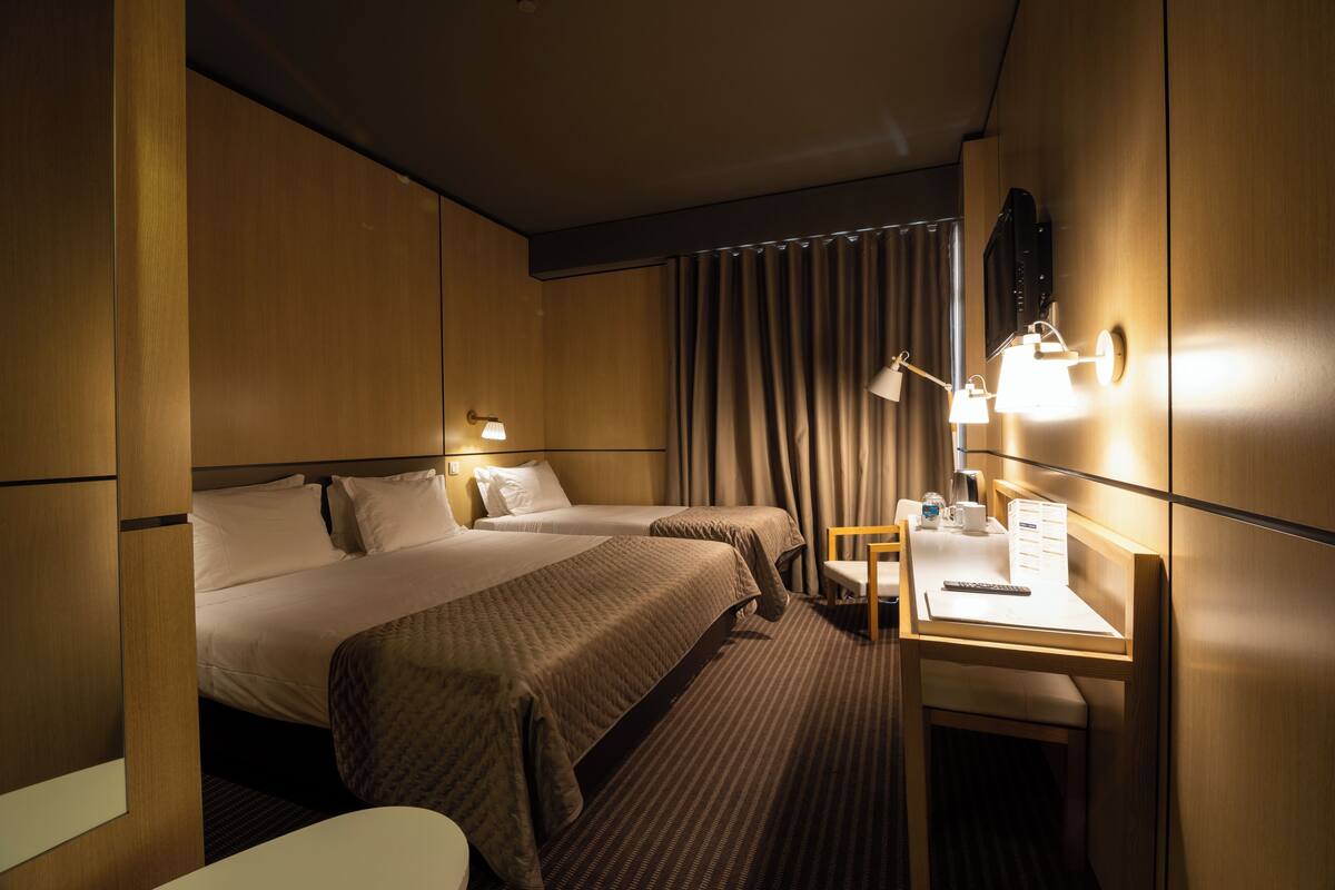 A hotel room with two beds, a desk with a chair, and a window with curtains.