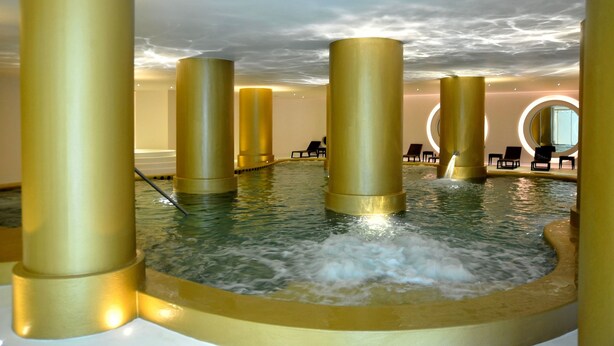 A spa area with a hot tub surrounded by golden pillars, lounge chairs, and a circular mirror on the wall. - Axis Vermar Conference & Beach Hotel (Povoa De Varzim)