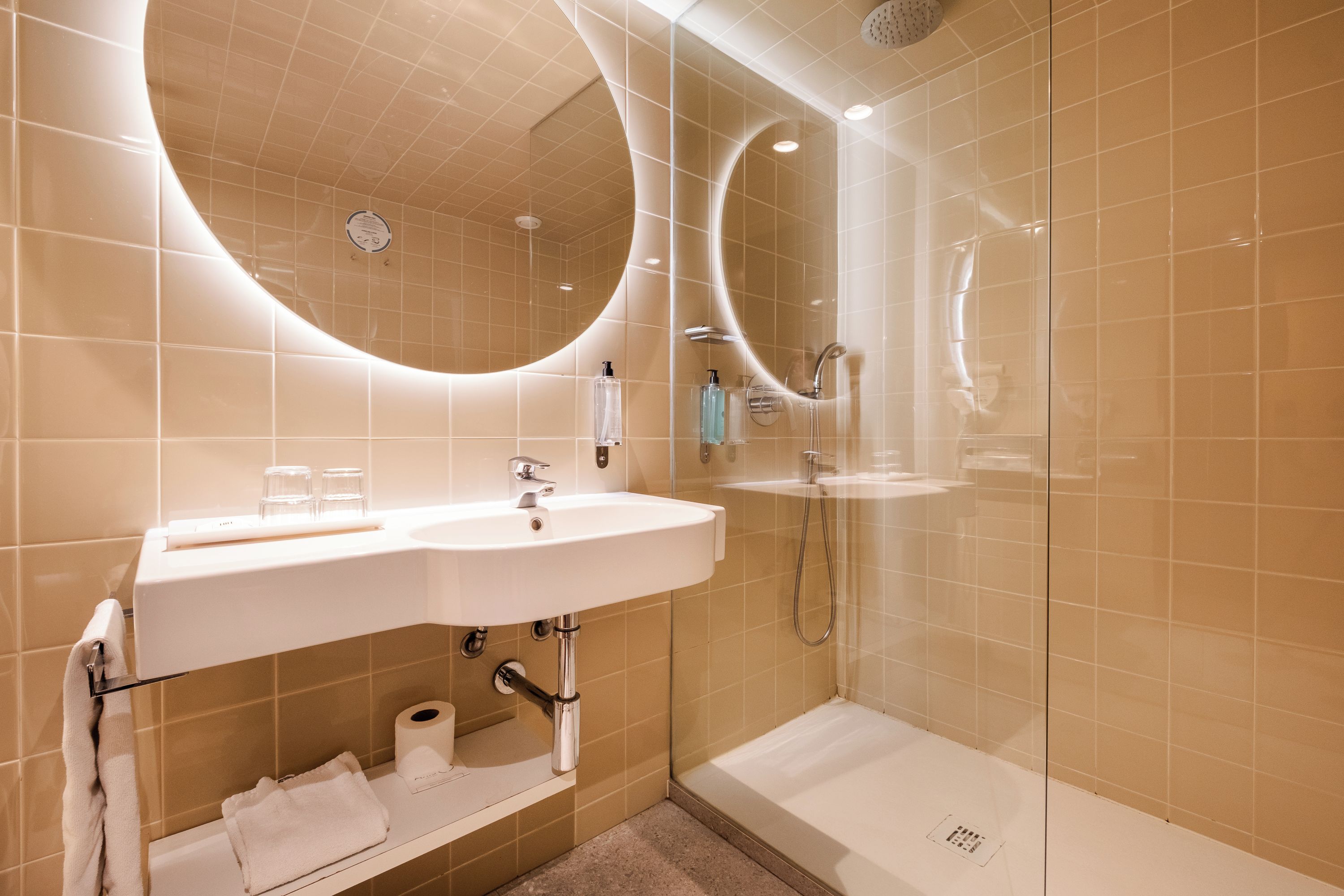 Un baño moderno con un espejo grande, un lavamanos y una ducha.