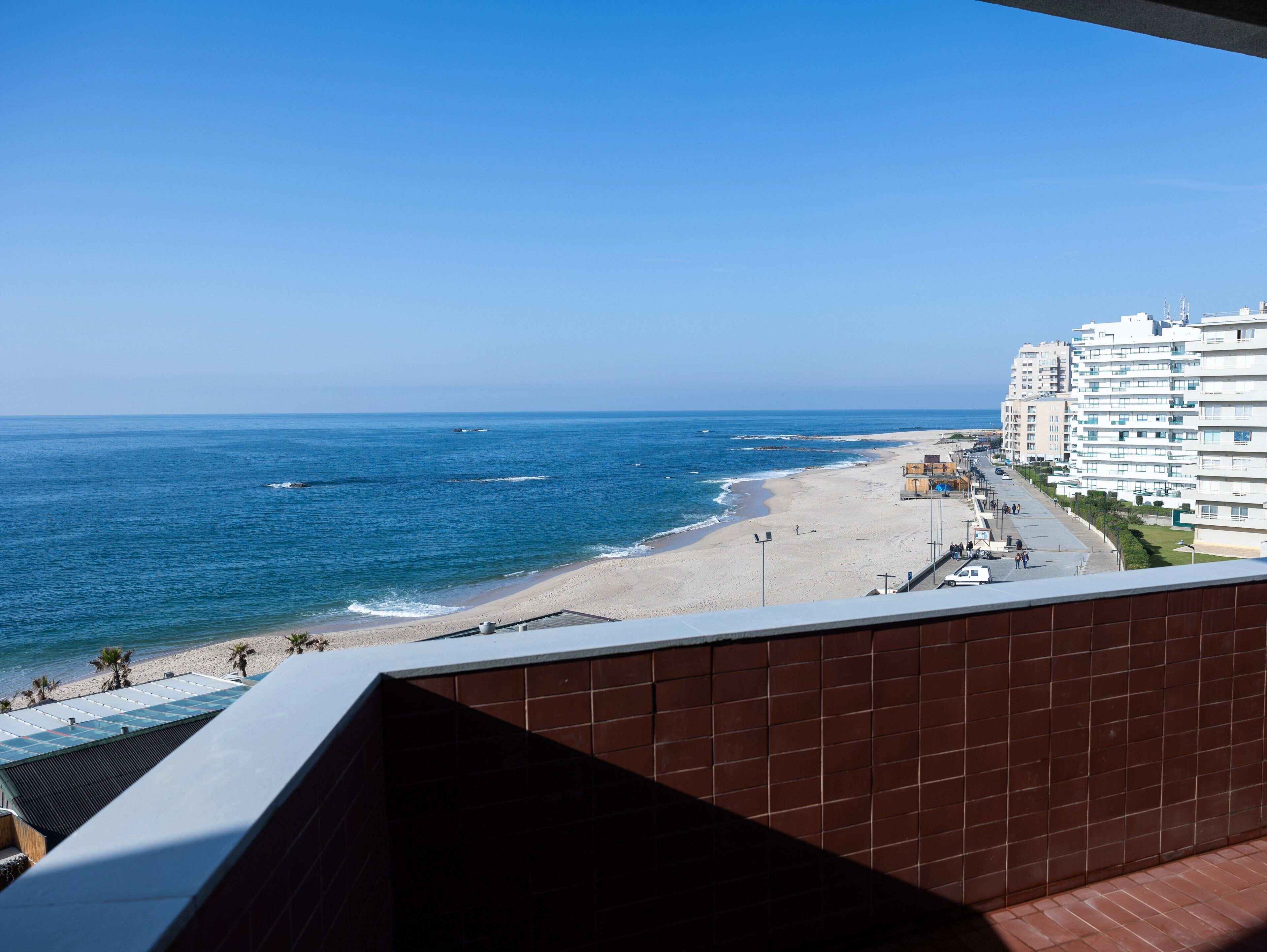 Vista costeira a partir de uma varanda com vista para uma praia e uma fileira de edifícios modernos.