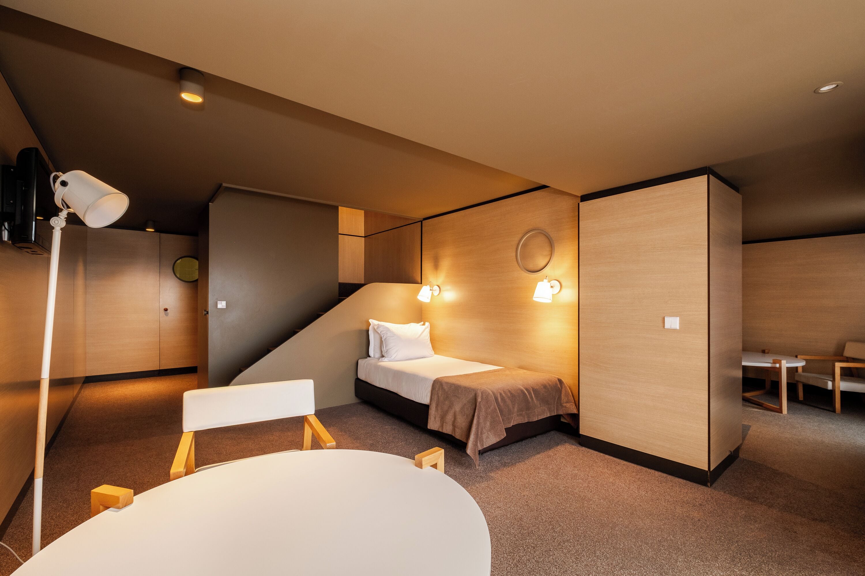 A modern hotel room with a bed, bedside table, and a desk area.