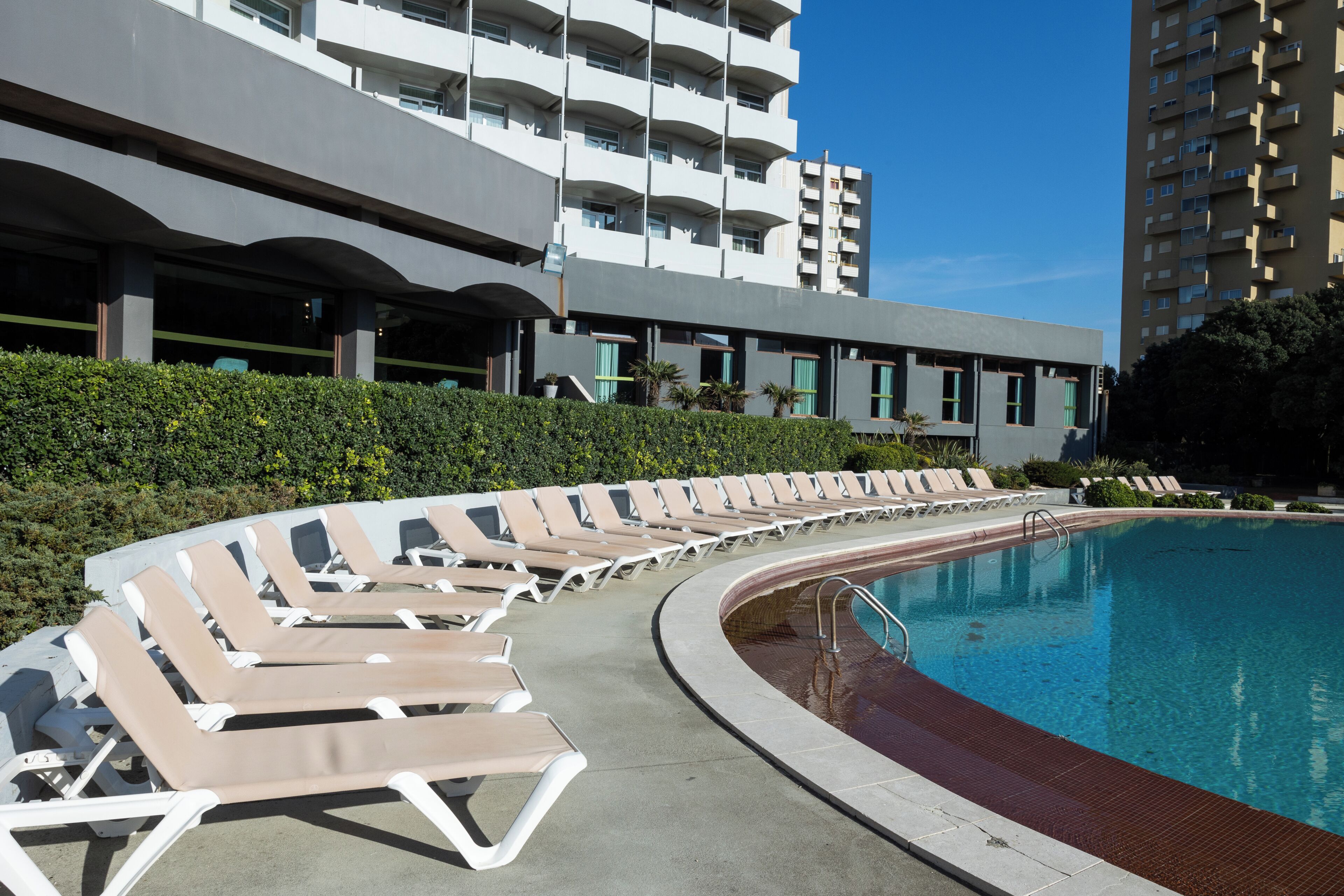 Ein Poolbereich mit Liegestühlen, einem Schwimmbecken und modernen Gebäuden im Hintergrund.