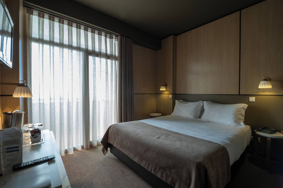 A hotel room with a large bed, bedside lamps, a desk with a lamp, and a window with curtains.