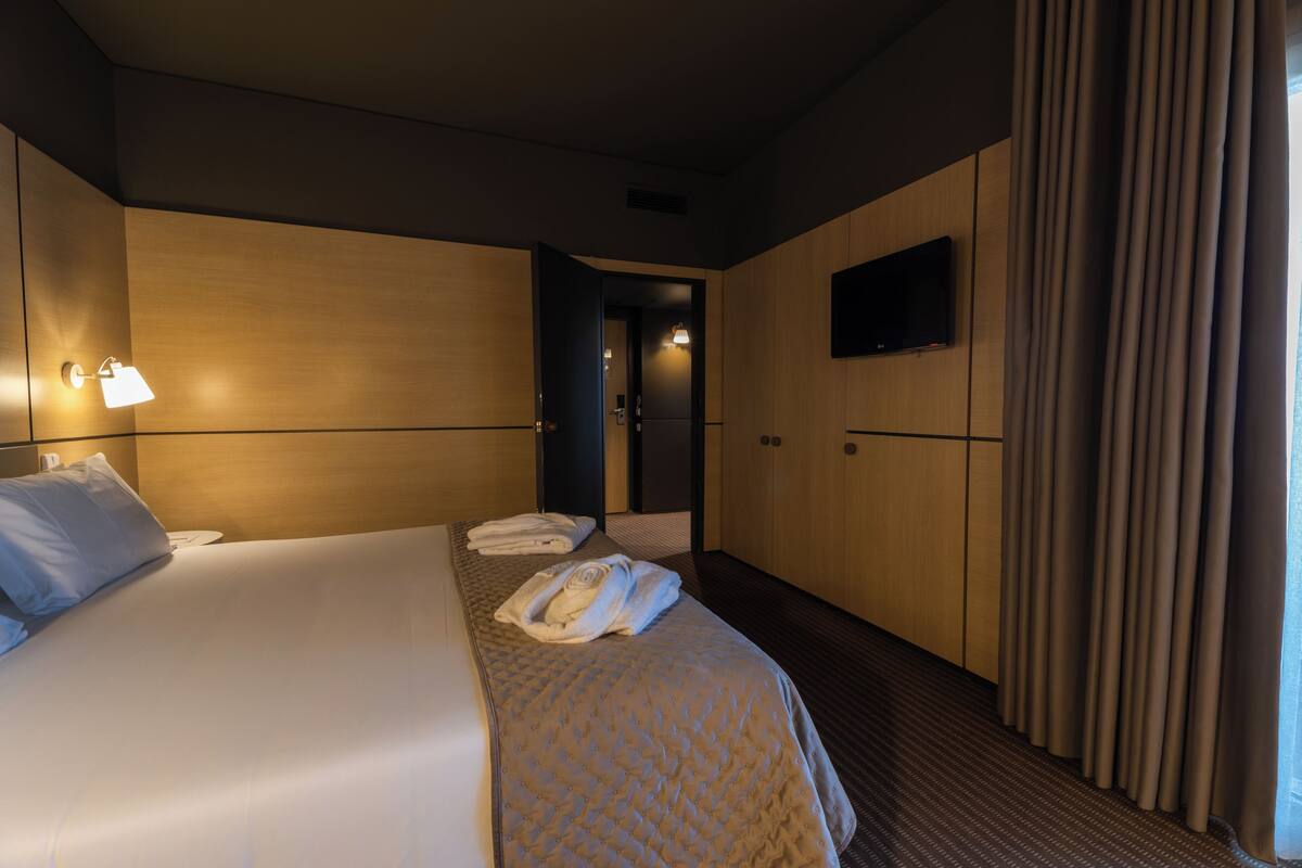 A hotel room with a large bed, a flat-screen TV mounted on the wall, and a door leading to a bathroom.