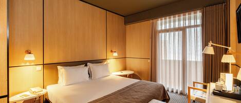 A hotel room with a large bed, bedside tables, a desk with a chair, and a window with curtains.