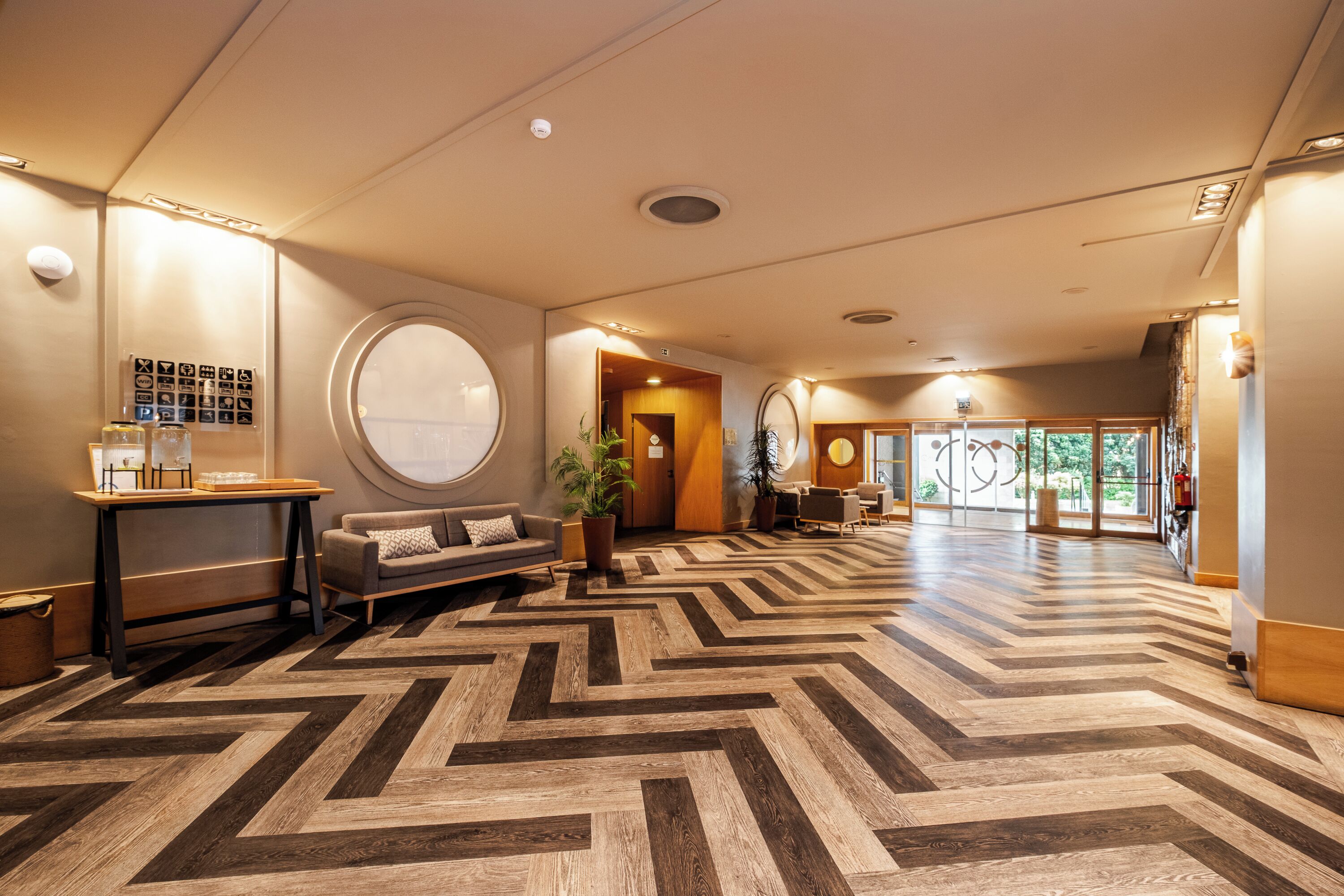 Et hotel lobby med et fiskebensmønstret gulv, en receptionsdisk, en sofa og et stort vindue.