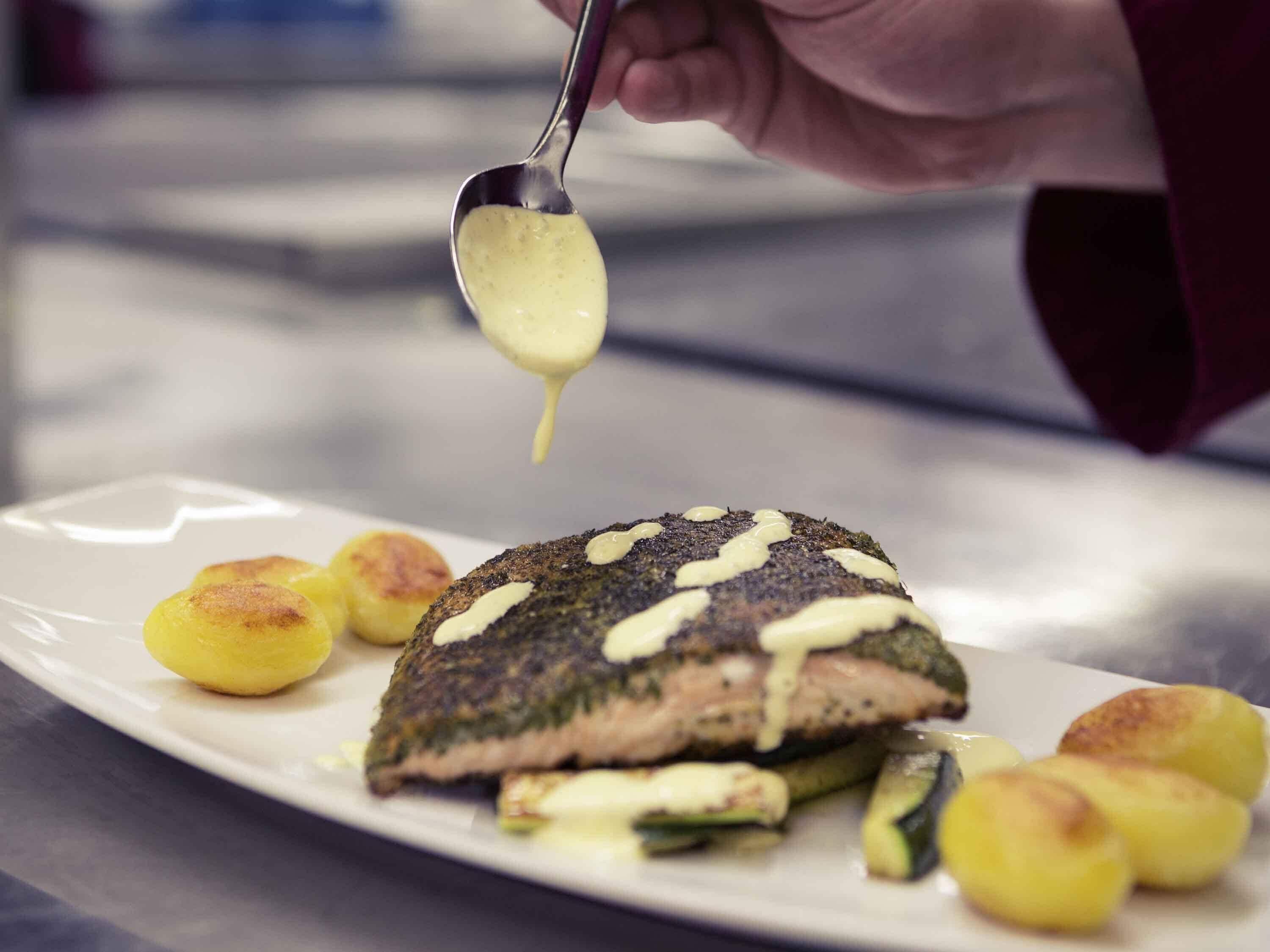 Ein Teller mit gegrilltem Fisch, der mit einer cremigen Soße überzogen ist, zusammen mit gerösteten Kartoffeln.