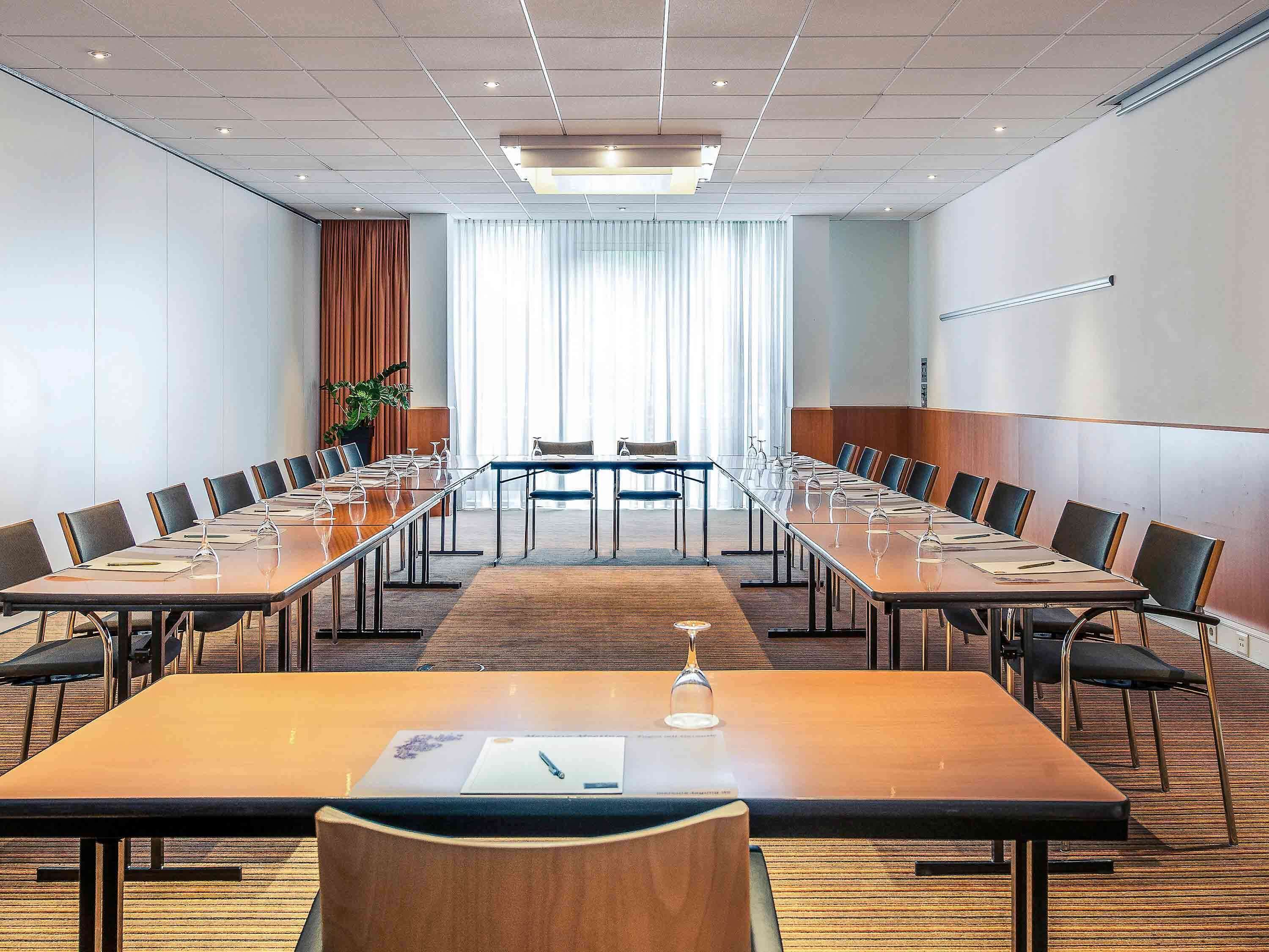 A conference room with long tables, chairs, and a large window with curtains.