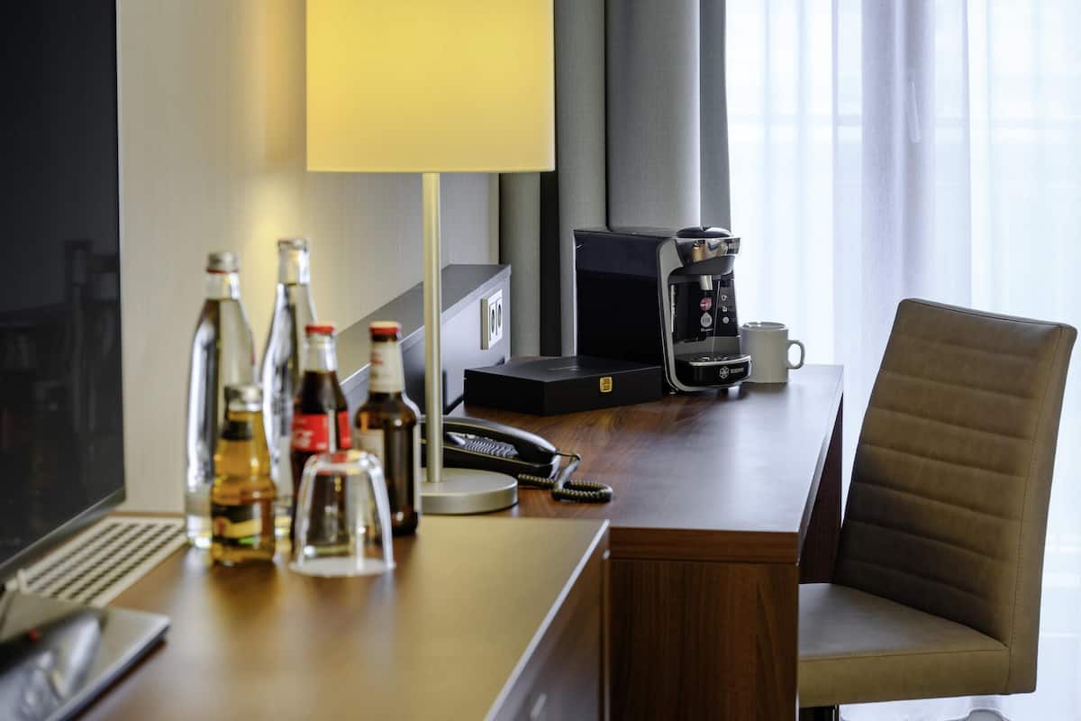 Une chambre d’hôtel équipée d’un bureau, d’une machine à café, d’une lampe, d’une chaise et d’un ordinateur.